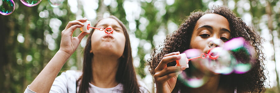 Two girls next to each other blowing bubbles at the camera
