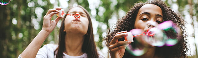 Two girls next to each other blowing bubbles at the camera