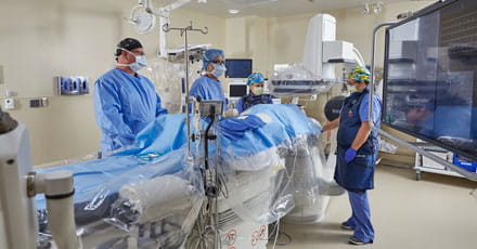 Image of a catheterization lab with 4 medical professionals providing treatment. 