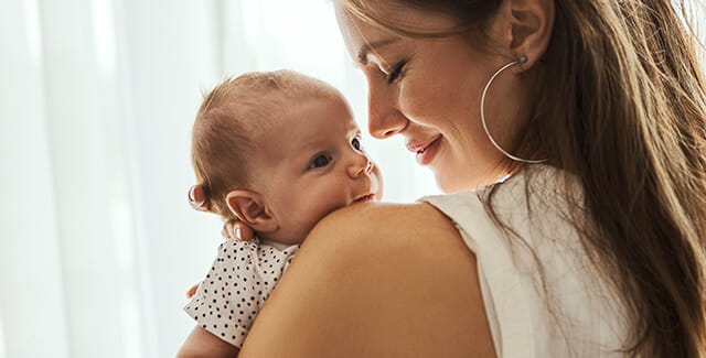 A mother smiles while looking down at her infant. Learn more about maternal health.