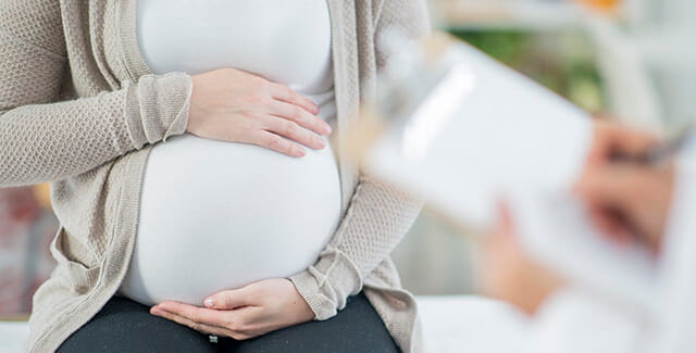 A pregnant woman rests her hands on her stomach. Learn more about maternity services.