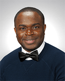 Onome wears a black sweater and a white collared shirt. He has a black bow tie.