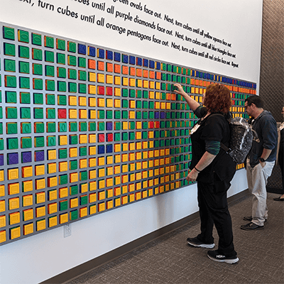During the planning stages for the artwork in the facility, Dr. Gwendolyn Sowa shared her vision for this reception area. She wanted artwork that would inspire social connections, play, and collaboration. In this photo, three people work together to turn the cubes.