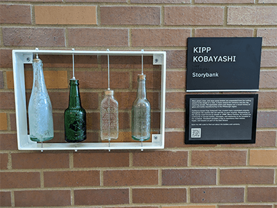 A  touch display of four bottles made in the Pittsburgh region is positioned near the midpoint of the corridor.