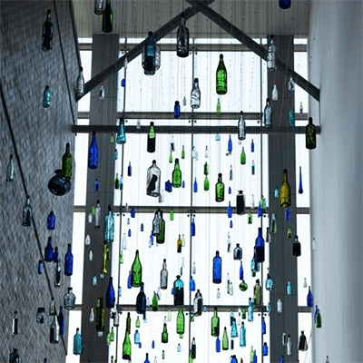 Blue, green, and white bottles suspended from a ceiling referencing Pittsburgh’s rivers and history of glass manufacturing. Learn more about the art installation Storybank by Kipp Kobayashi.