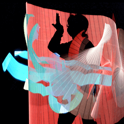 Interwoven streams of red and blue light cross over the silhouette of a woman holding an LED light stick. She is standing in front of a black background.