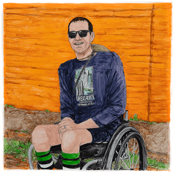 Bryan sits in a wheelchair front of an orange wall. 