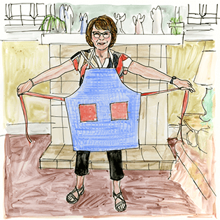 Linda stands in front of a fireplace wearing a blue apron with red pockets.  