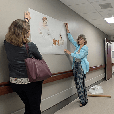 Sandy developed three different paintings that portray historic and contemporary conversations about building the hospital, patient care, and community volunteers. In this photo, the artist is deciding on the scale and location of the paintings. 