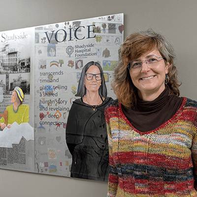 The artist posing in the hallway after a successful installation! In this painting, the artist contrasts historic volunteers who sewed bedsheets for patients with a contemporary community member who gives their time and expertise to the hospital. 