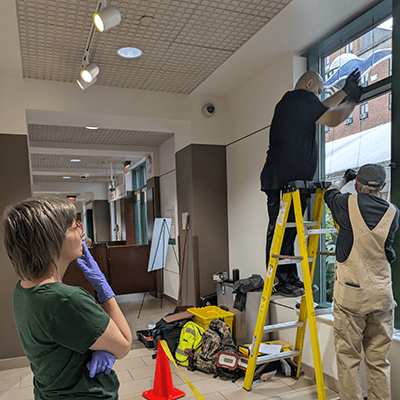 The artist hired Extech Exterior Technologies, based in Sharpsburg, to install her project.  Here, she watches as the first pieces are carefully hung from the window frames. 