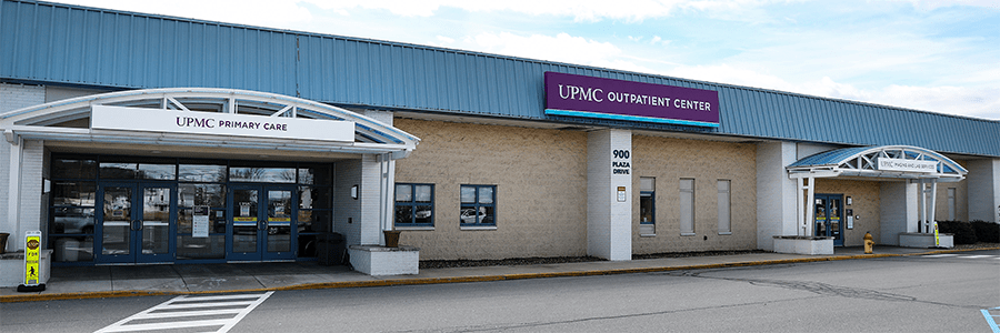 The exterior of UPMC Outpatient Center. There is a large yellow brick building with a purple sign which reads: "UPMC Outpatient Center".