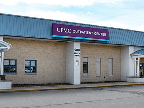The exterior of UPMC Outpatient Center. There is a large yellow brick building with a purple sign which reads: "UPMC Outpatient Center".