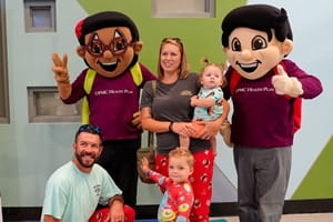 Smiles all around as a family pose with UPMC Health Plan mascots at the NICU Reunion Pajama Party.