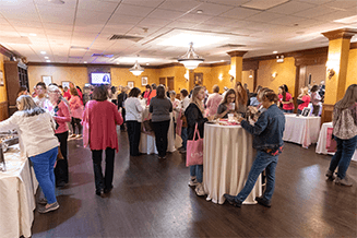 A room full of Pretty in Pink goers enjoy food and refreshments while visiting vendors’ tables.