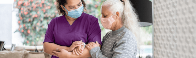 A nurse wearing purple scrubs helps a woman.