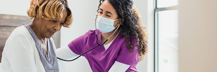 A woman with purple scrubs takes an older woman's blood pressure.