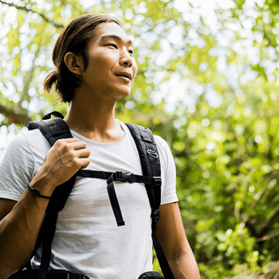A man is hiking. He has a backpack. He wears his long hair tied back.