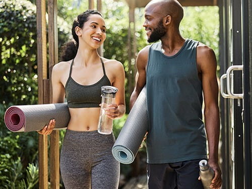 Image of man and woman walking with yoga mats.