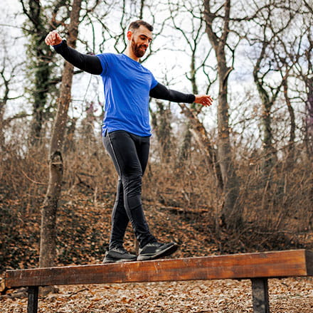 A man balances on a beam on a hiking trail.