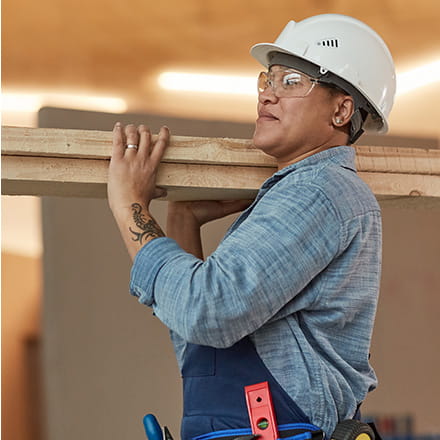 A construction worker carries lumber across a worksite.