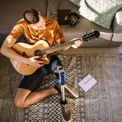 A man with a prosthetic leg sits on the floor playing an acoustic guitar.