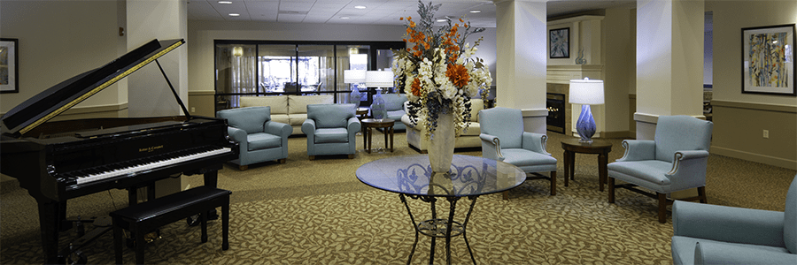 Blue lounge chairs surround a grand entry. There is a black concert piano in the room's corner. A vase of bountiful flowers is on a glass table.