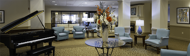 Blue lounge chairs surround a grand entry. There is a black concert piano in the room's corner. A vase of bountiful flowers is on a glass table.