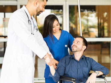Patient in wheelchair leaving the hospital thanking doctor and nurse