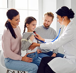 Doctor examens child surrounded by her parents