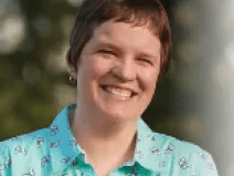 Karen wears a blue printed collared shirt that has butterfly details. Her hair is cropped short and is brown. She is smiling enthusiastically.