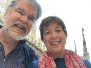 Mark Roberts has a gray well-trimmed beard. He has gray hair. He wears glasses. He is smiling. He has on a lab coat and blue collared shirt.