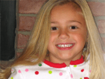 Hayley has long blonde hair that goes beyond her shoulders. She is tan. She is smiling and wearing rainbow polka-dot pajamas. 