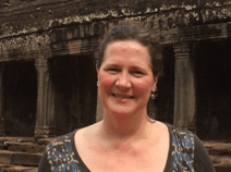 She wears a floral blouse with a black background. She has earrings. Her brown hair is in a bun.