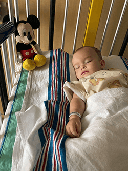 Kai with a Mickey Mouse stuffed animal laying in the hospital