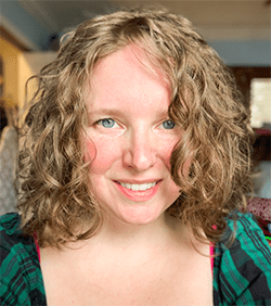 Bianca has light brown wavy, shoulder length hair. It frames her face. She is smiling and has bright blue eyes.